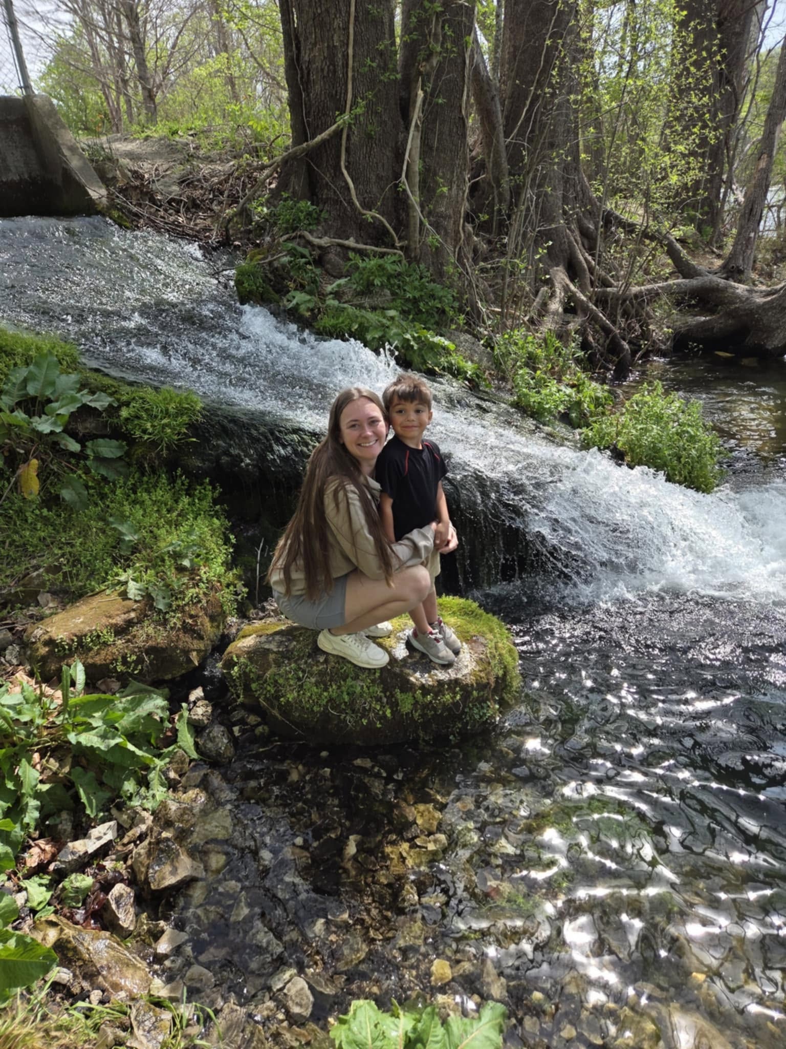 Jessica and her son crouched by a small waterfall in the woods