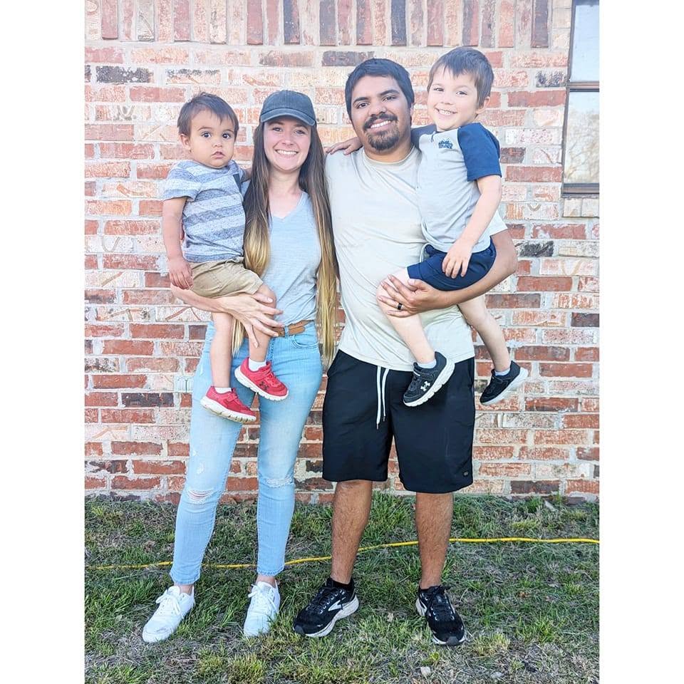 Jessica, her husband, and their two sons in front of a brick wall